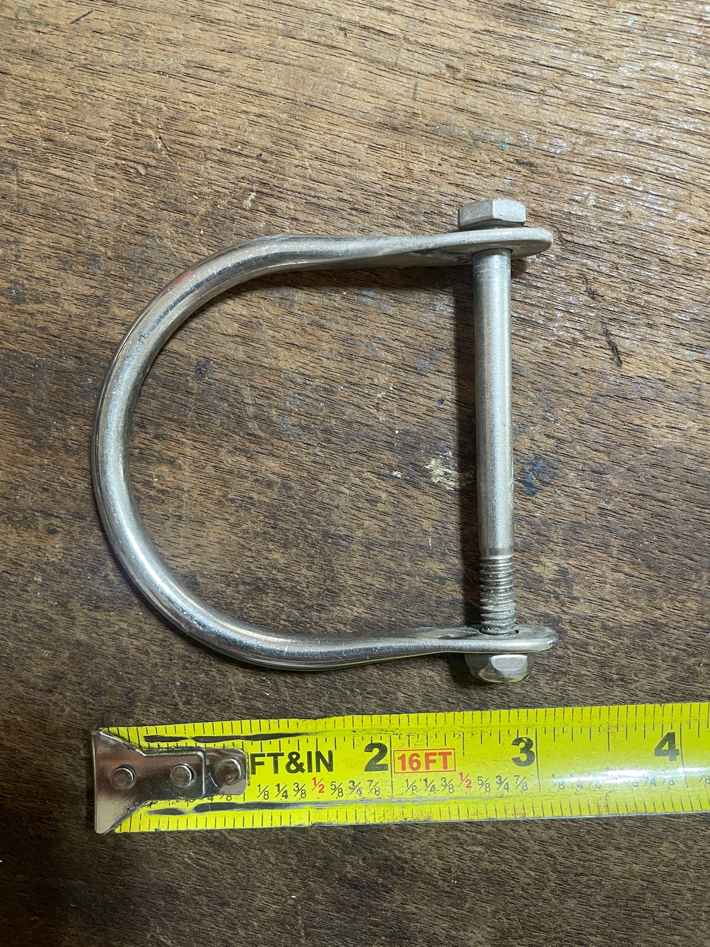 Metal U-bolt with a measuring tape on a wooden surface