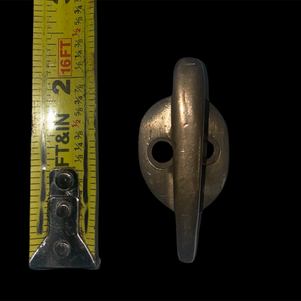 Metal cleat with a tape measure for scale on a black background