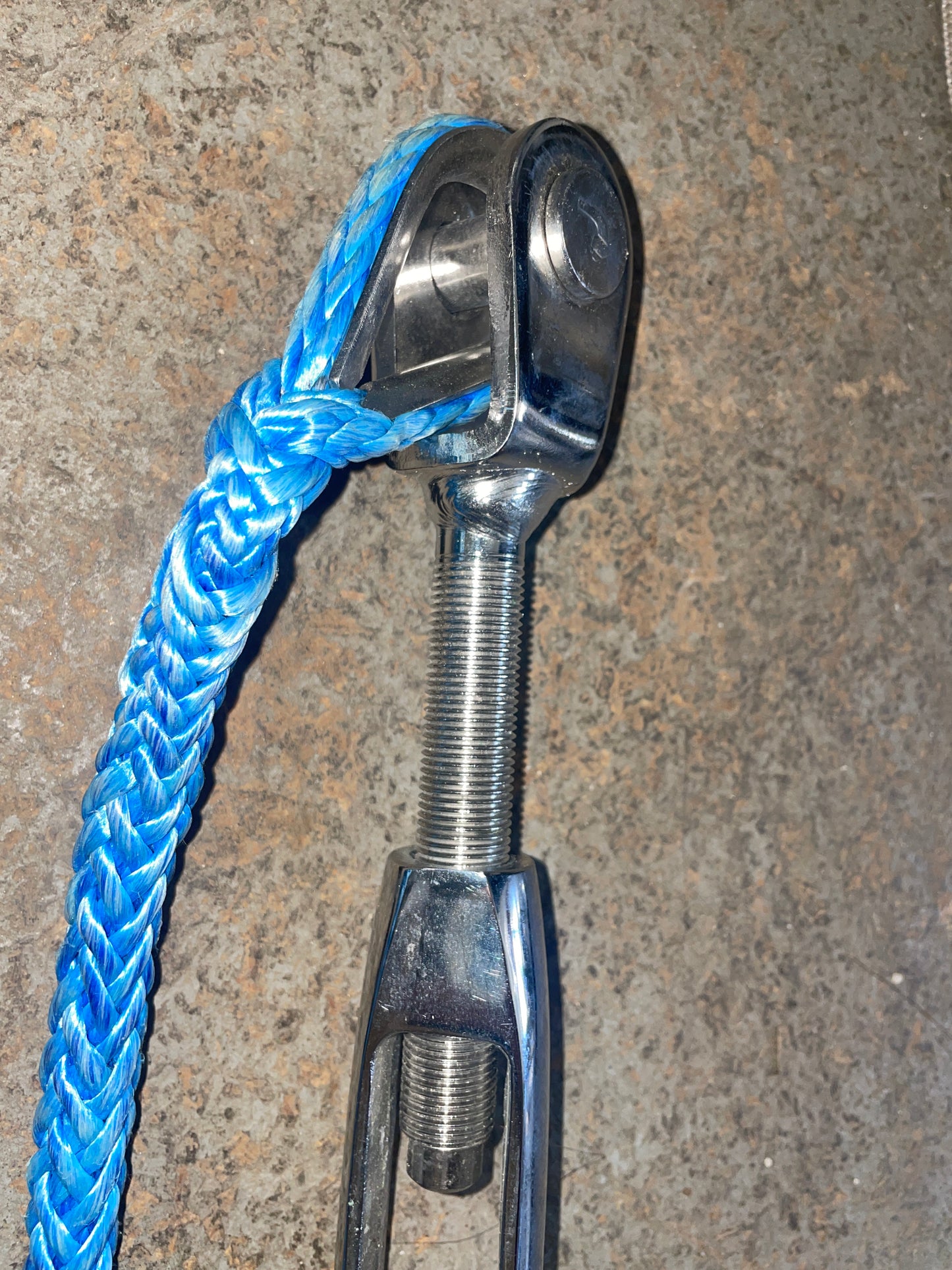 Metal clevis hitch with blue rope on a concrete surface