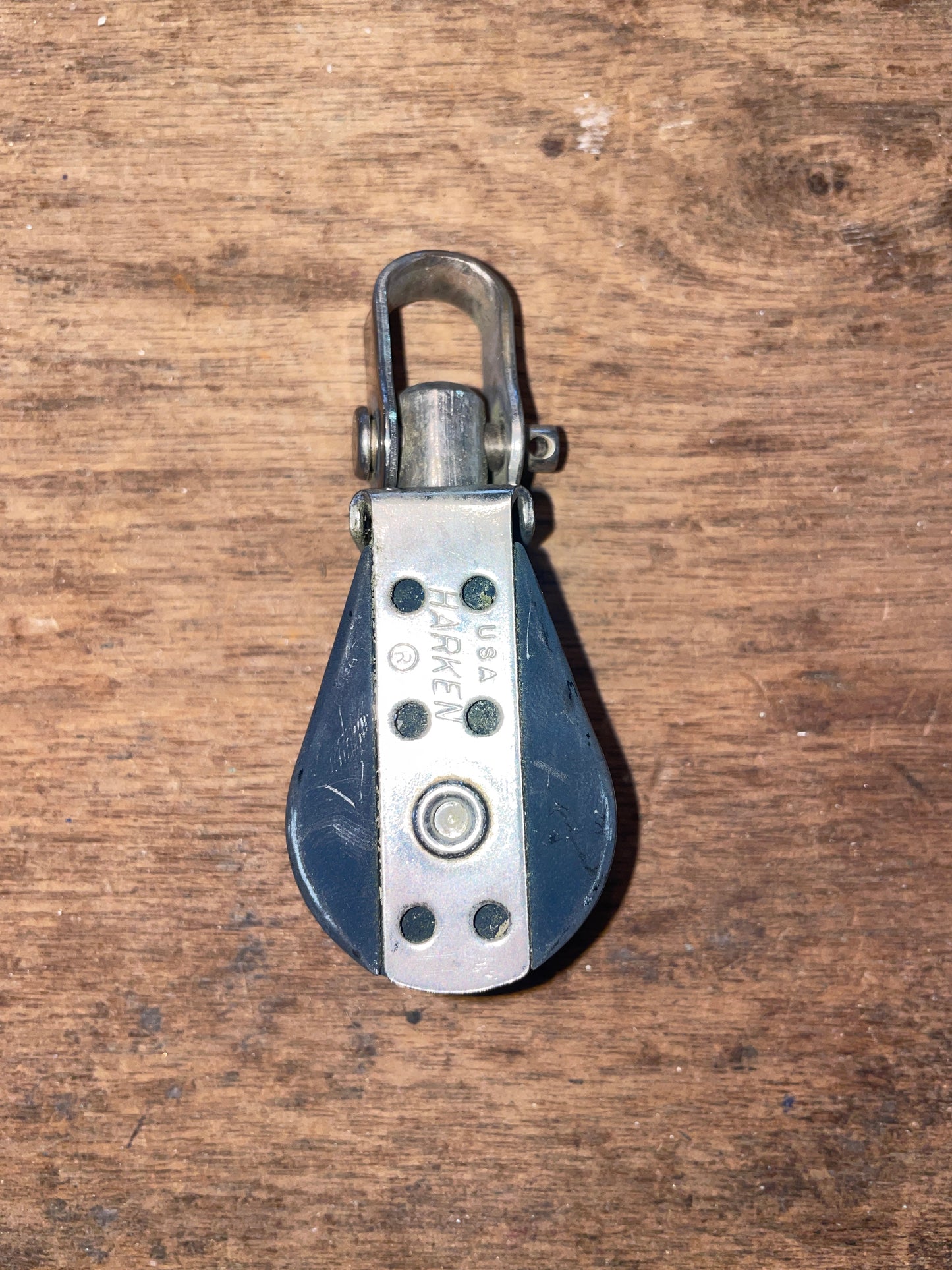 A small harken single swivel block with shackle, lying on a wooden surface.