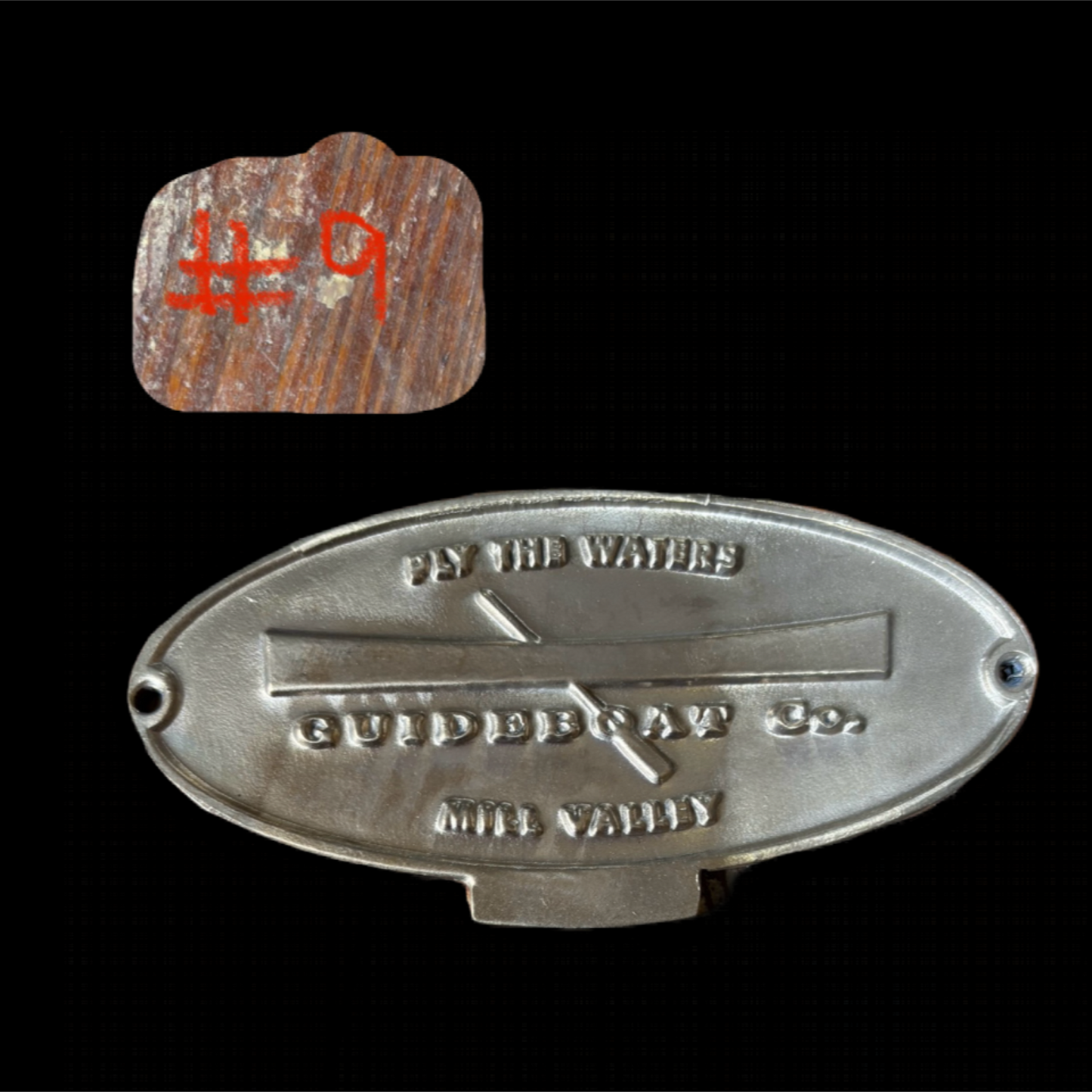 Metal badge with text and a wooden piece labeled '#9' on a black background