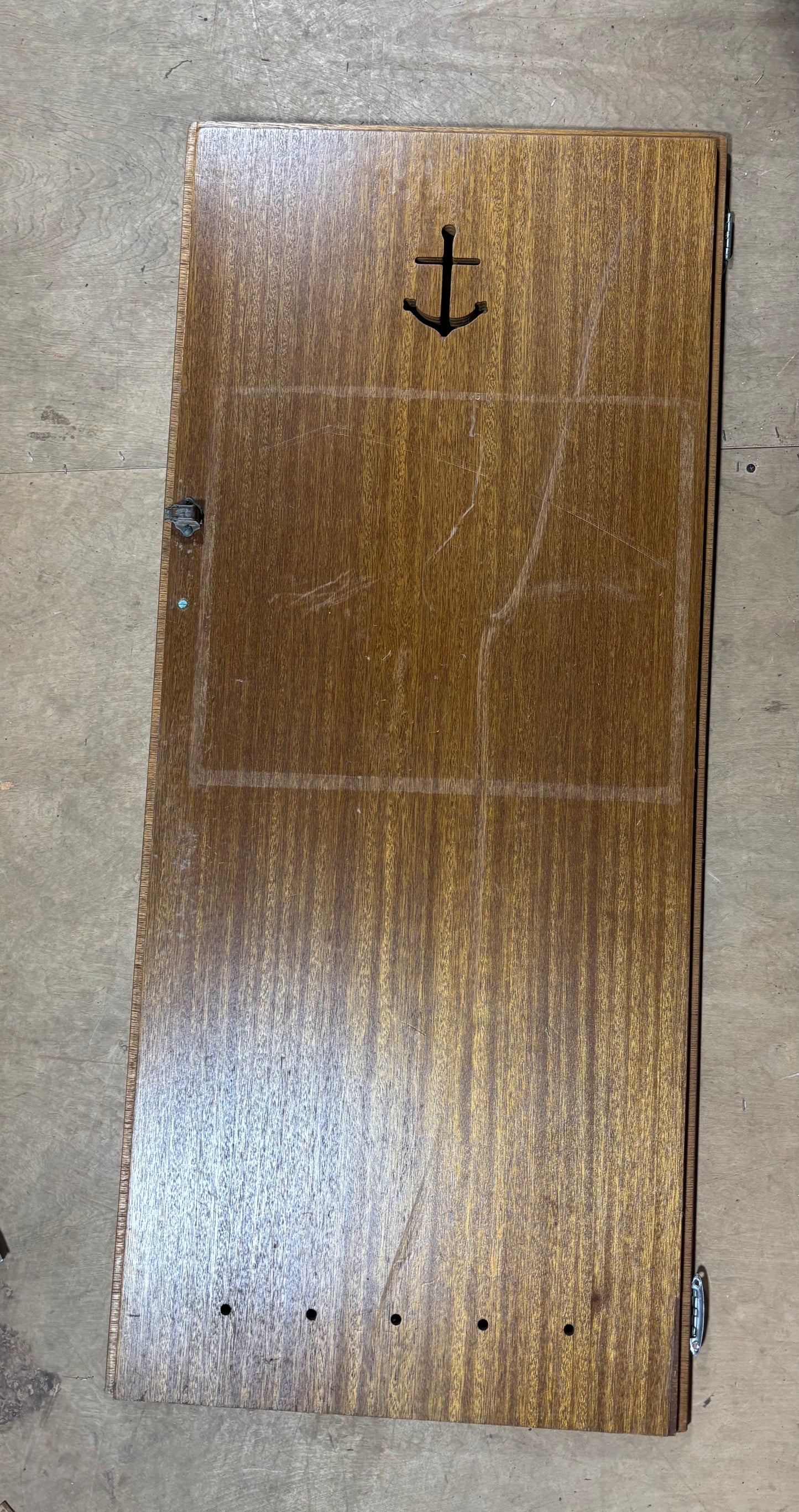 Wooden skateboard deck with an anchor design on a beige floor.
