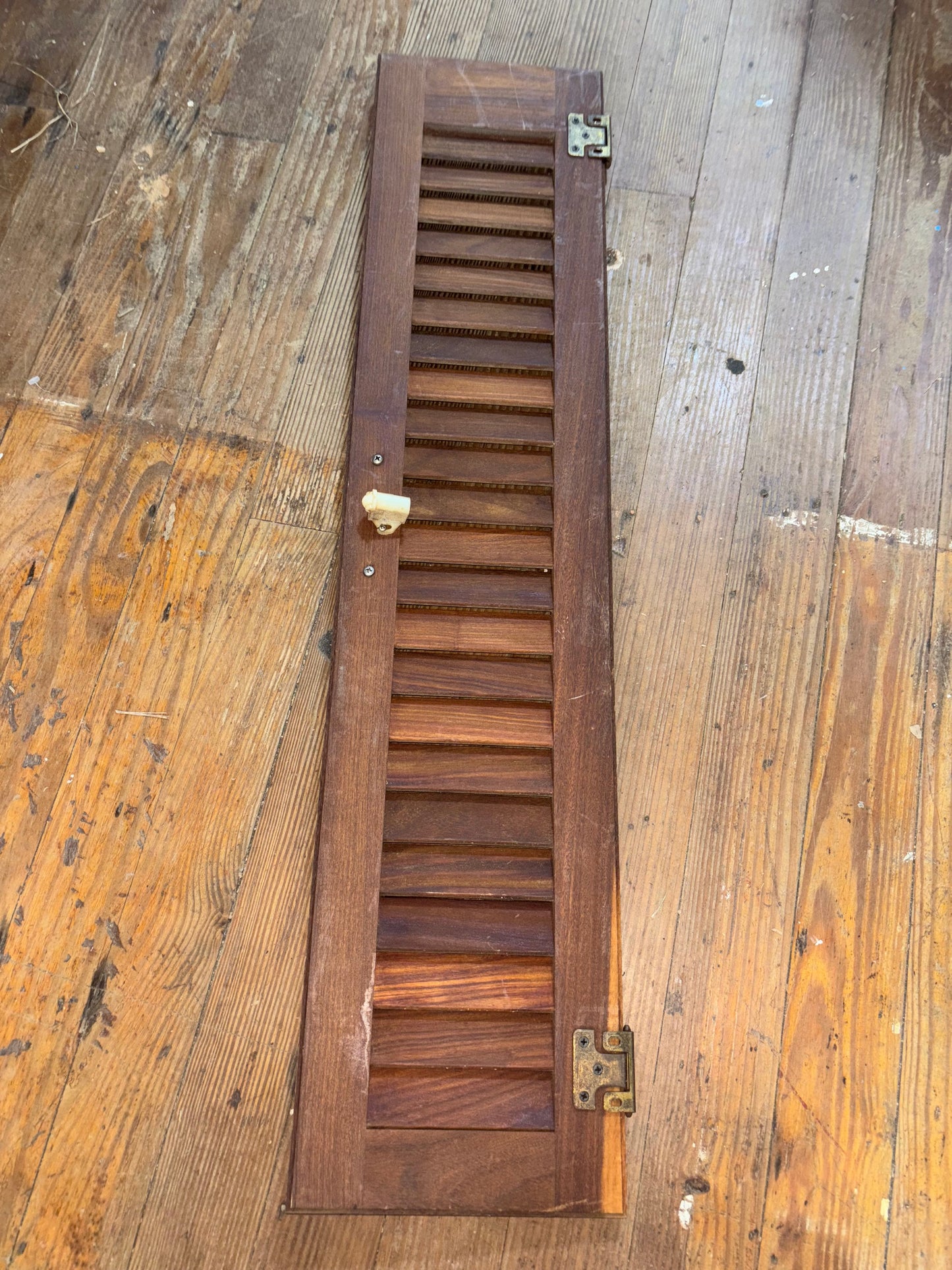 Wooden slatted panel with metal hinges on a wooden surface