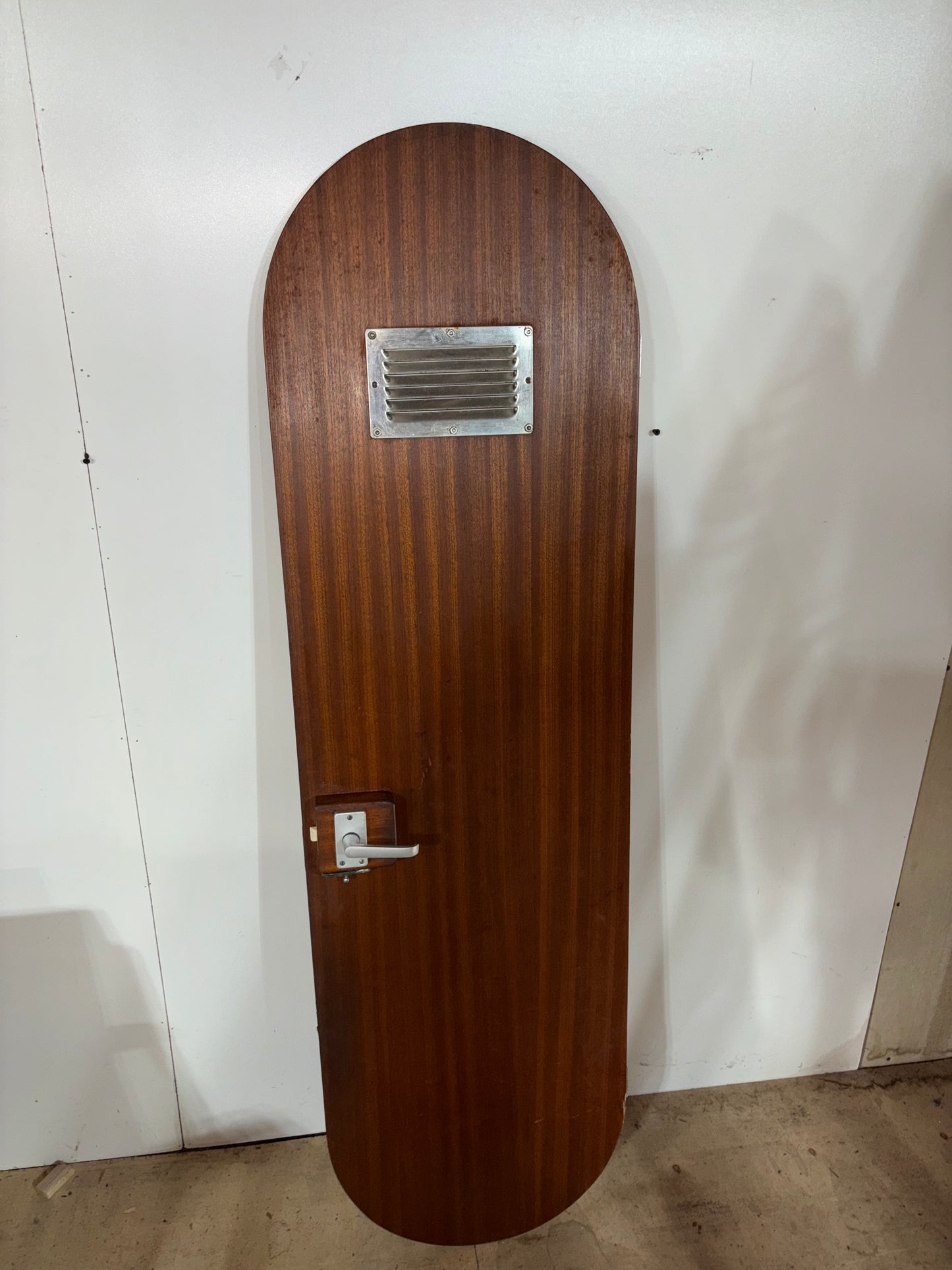 Wooden door with a metallic handle and vent on a white wall.