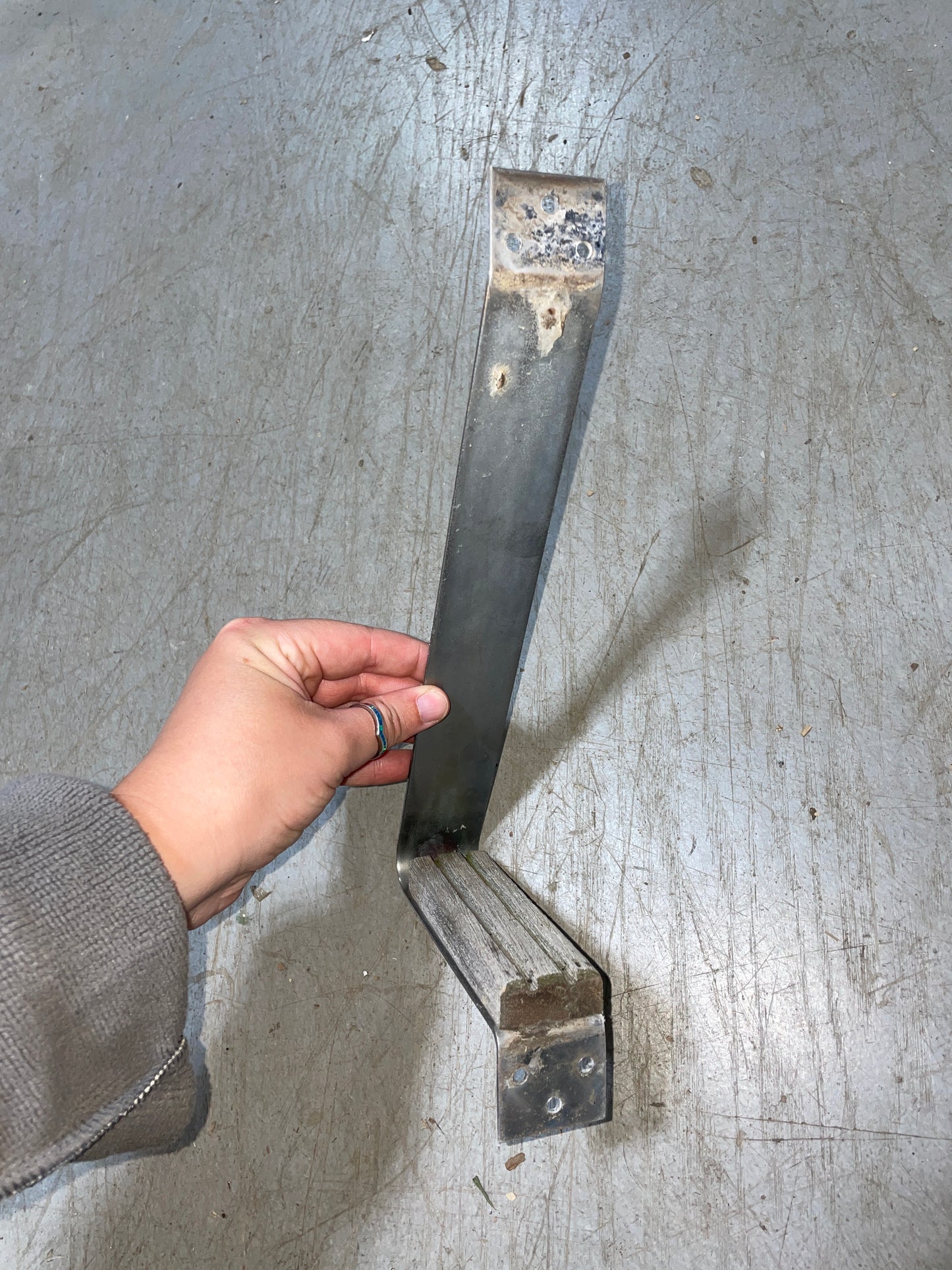 Metal bracket held by a hand on a concrete floor