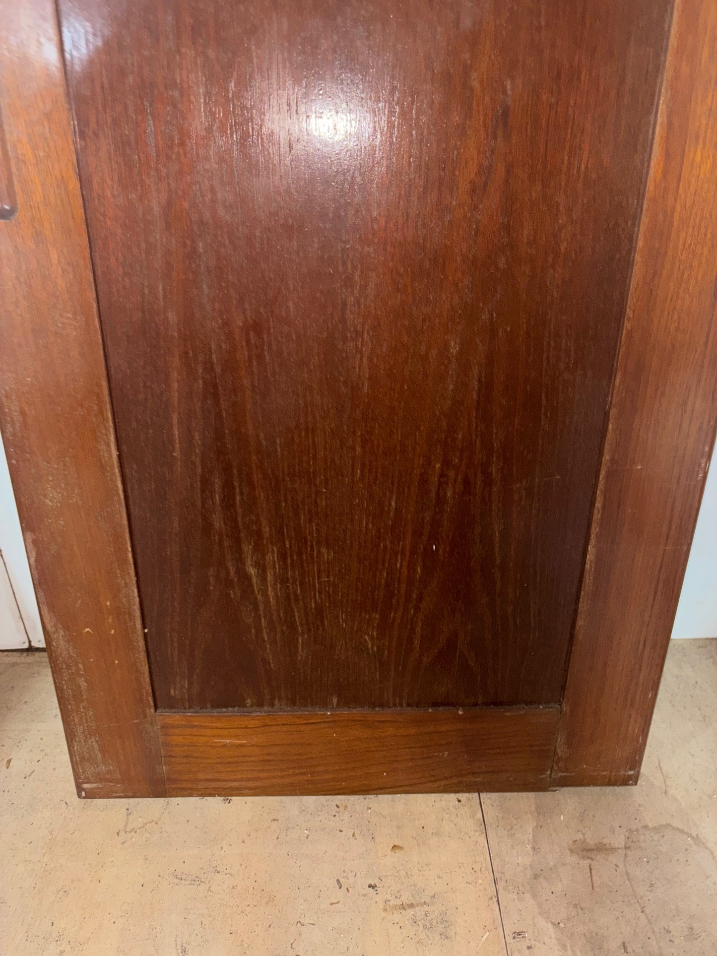 Wooden cabinet door with a visible scratch on a tiled floor.