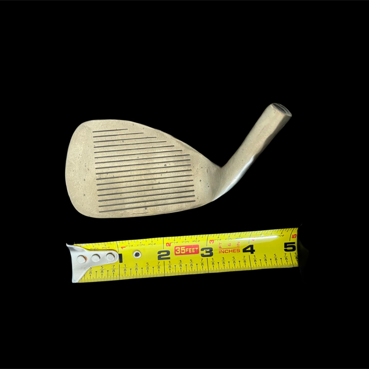 Golf club head with a measuring tape for scale on a black background