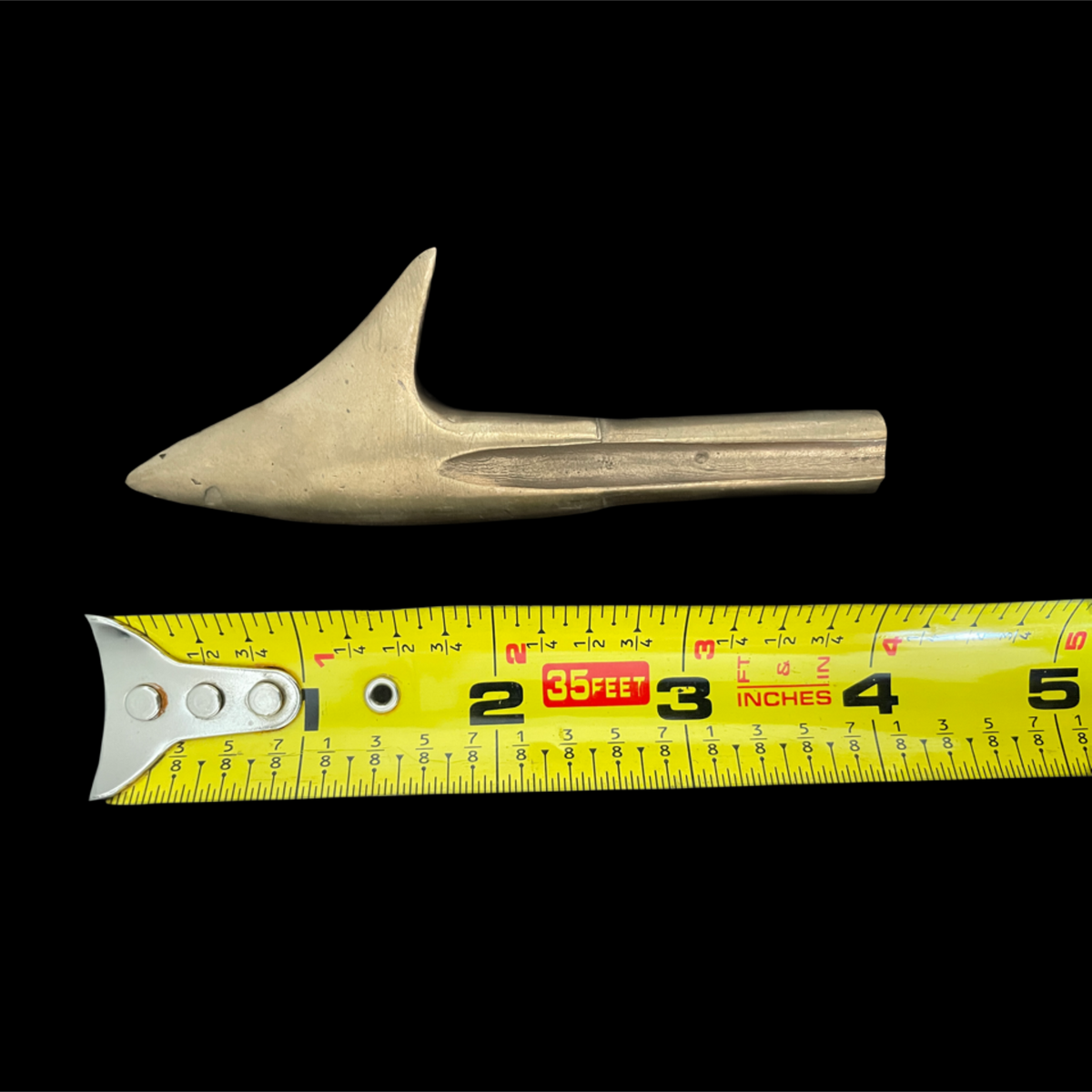 Metal tarpoon next to a measuring tape on a black background