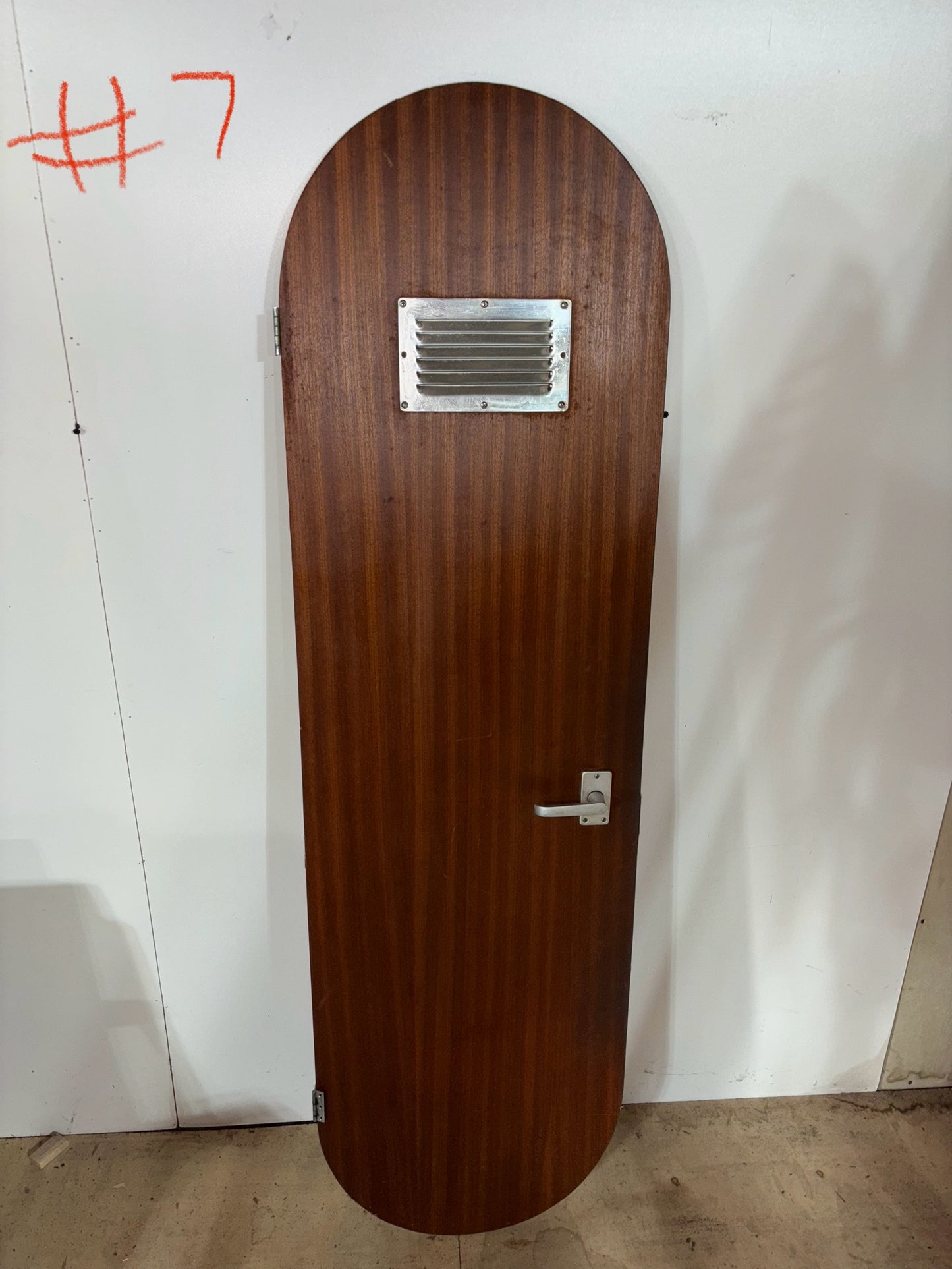Wooden door with a metal vent and handle on a white wall.