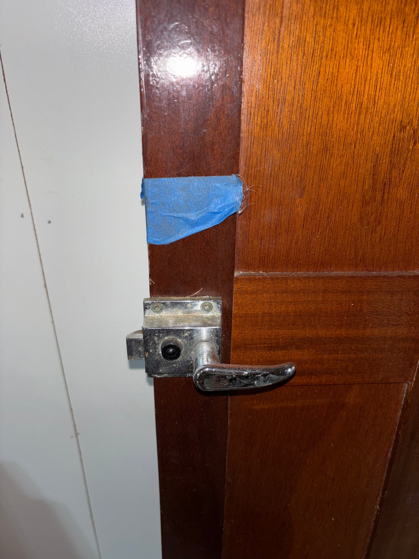 Wooden door with a metal handle and blue tape on a white wall.