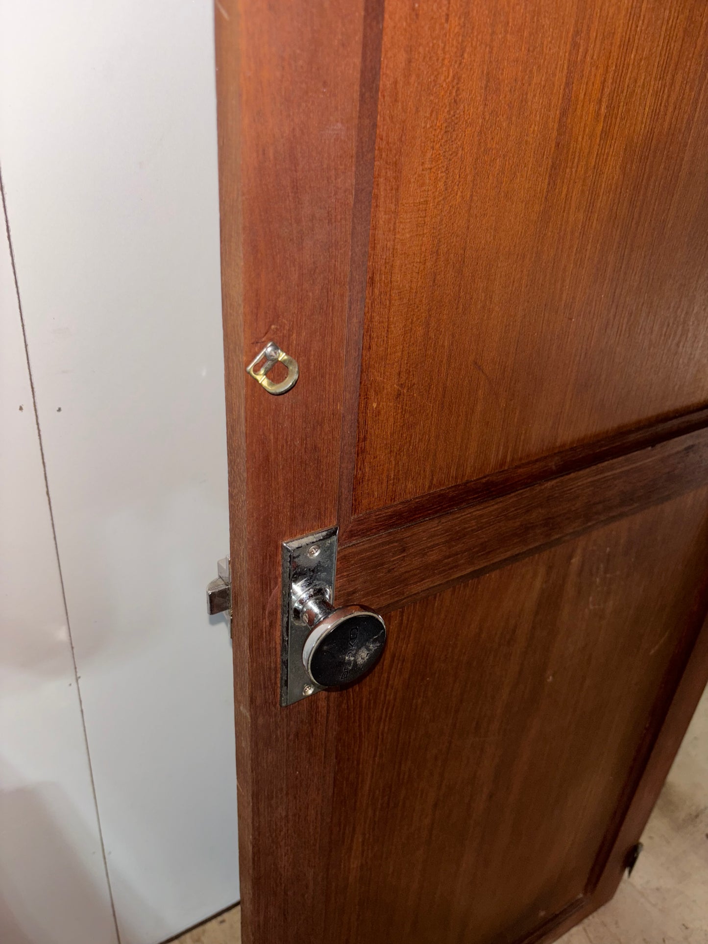 Wooden door with a metallic doorknob and lock on a white wall.