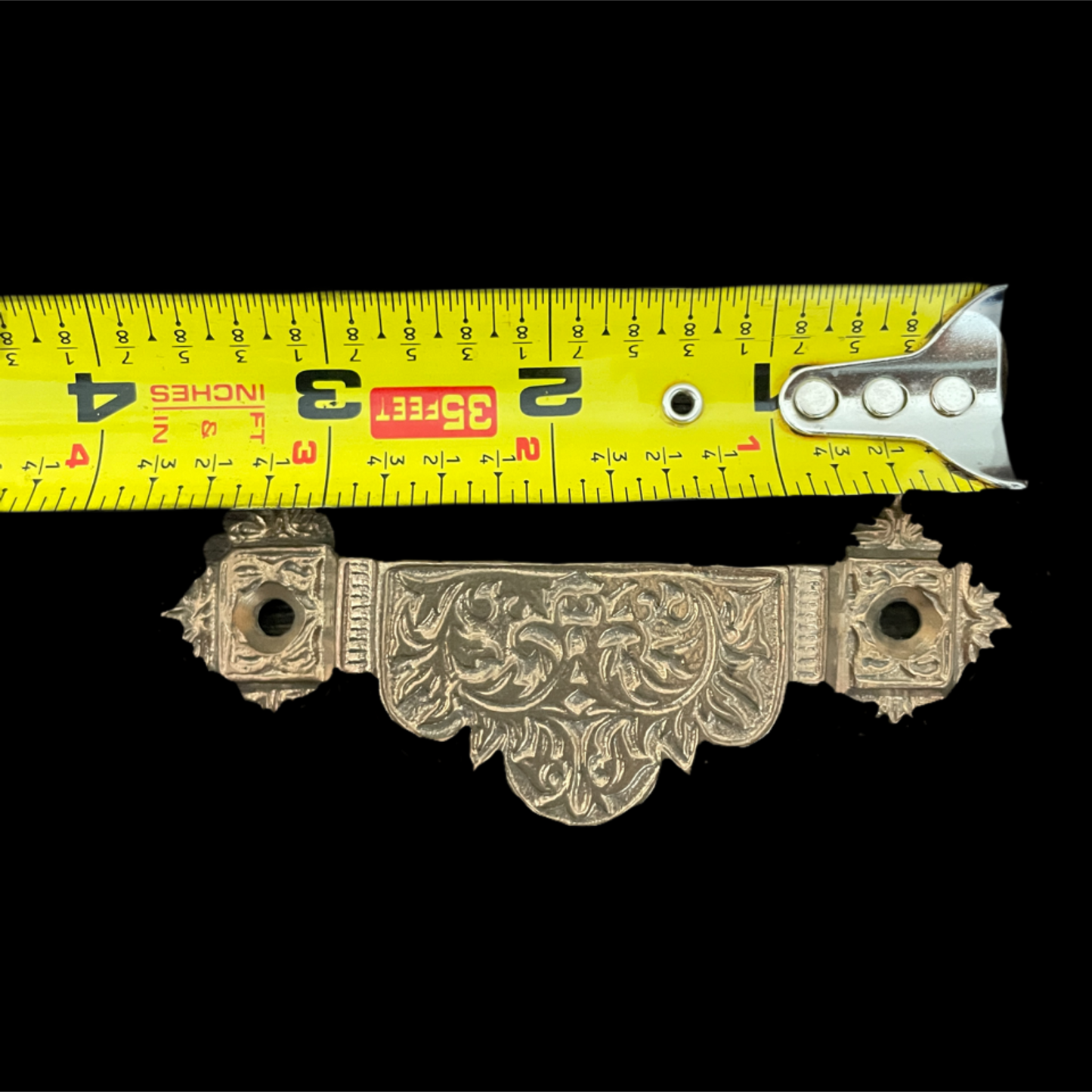 Decorative metal bracket with a measuring tape for scale on a black background