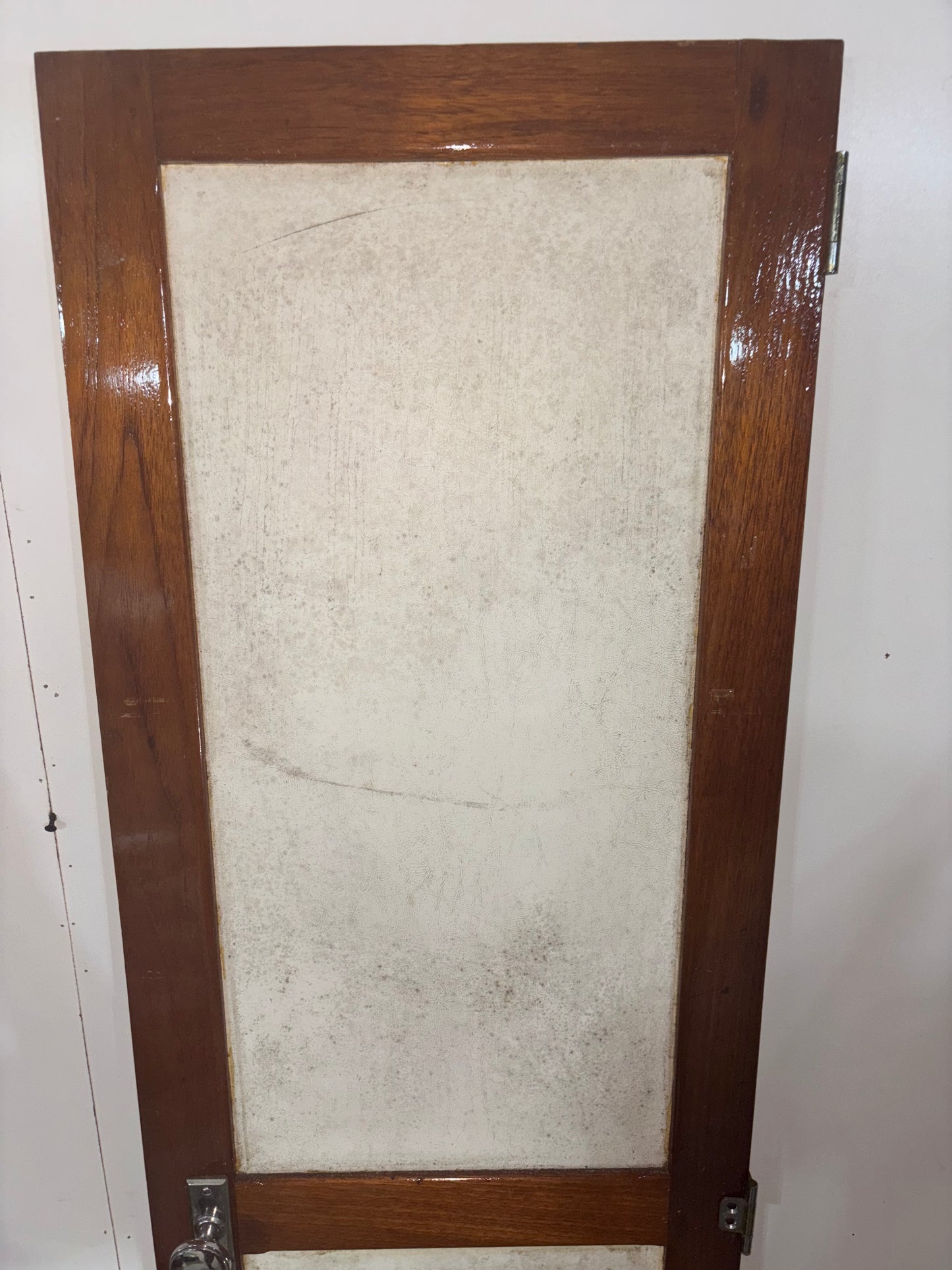 Wooden-framed mirror with a textured beige center on a white wall.
